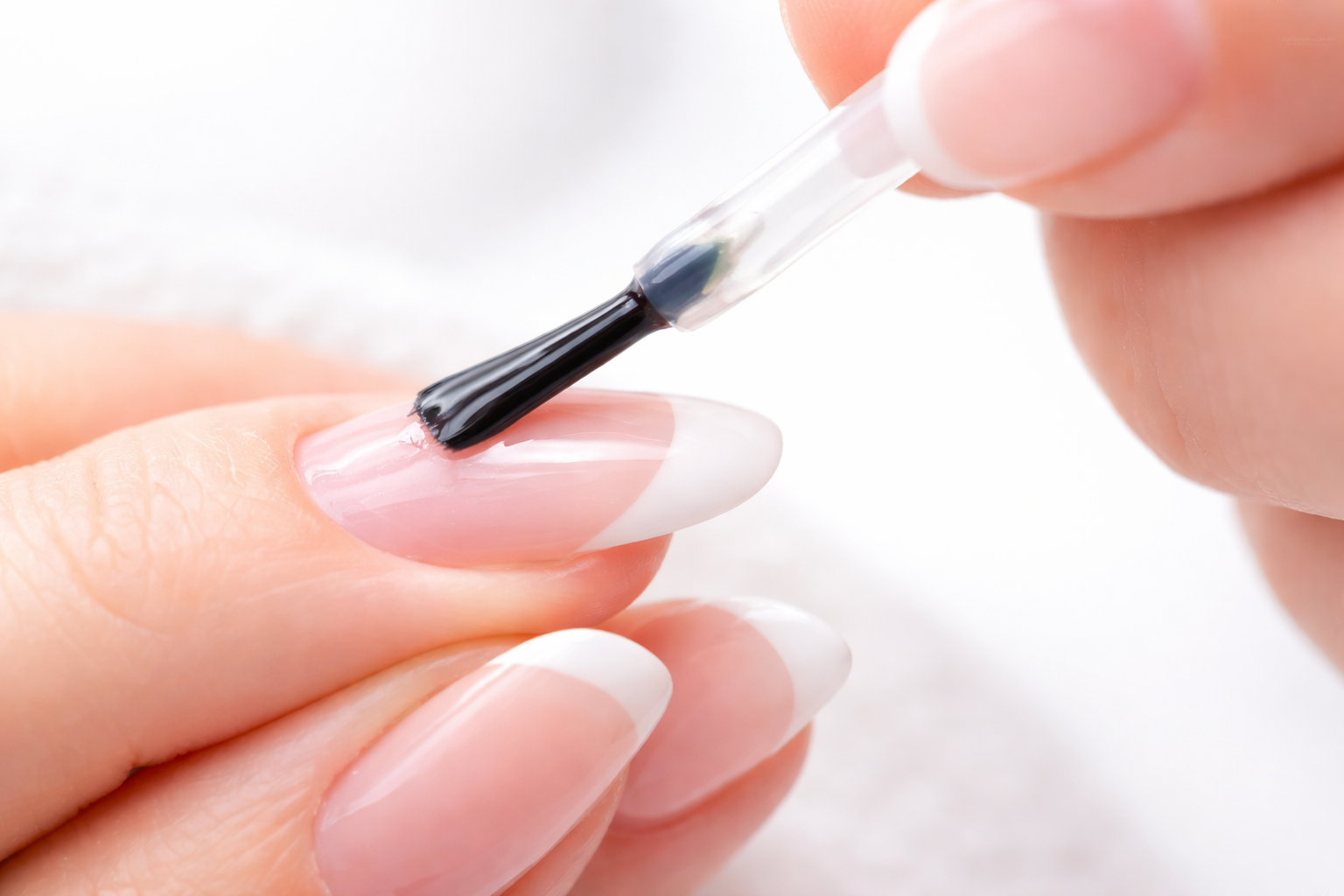 Close-up of a clear gel top coat being applied to a natural almond-shaped nail.