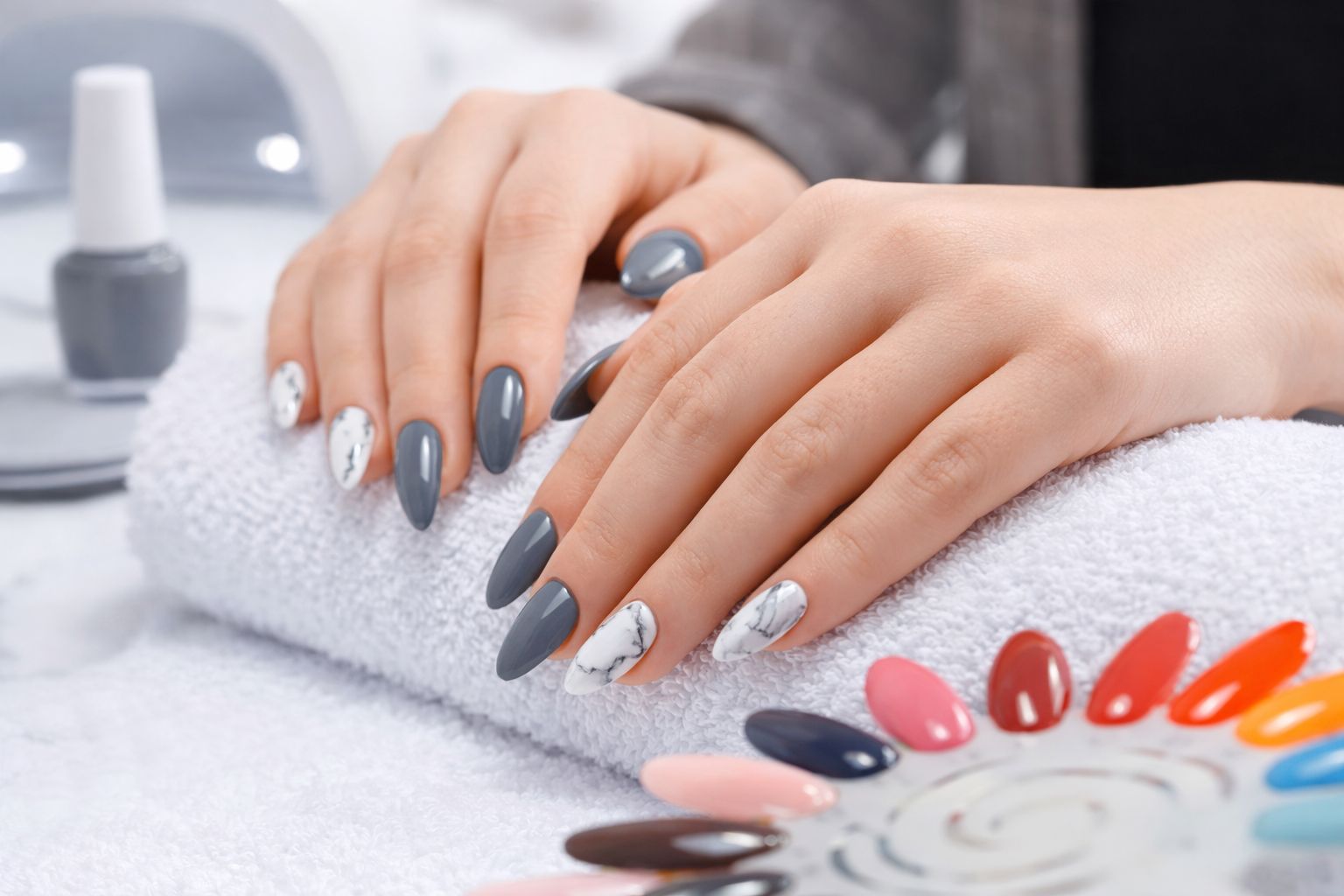 Modern almond-shaped gray gel nails with white marble accent design resting on a white spa towel.
